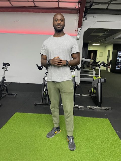 Coach certifié de Grind Fitness montrant des exercices de musculation dans la salle de sport.
